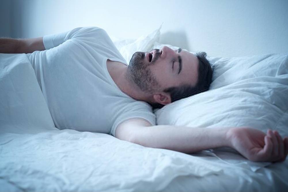 Man that suffers from sleep apnea symptoms lying in bed