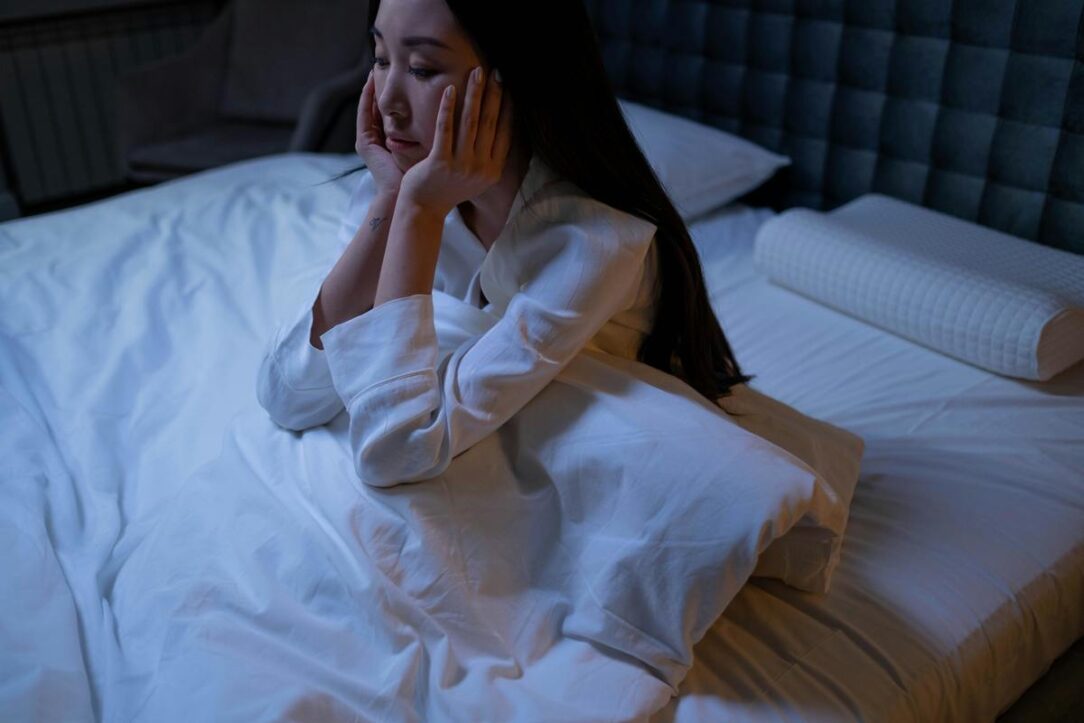 asian woman sitting up in bed due to insomnia